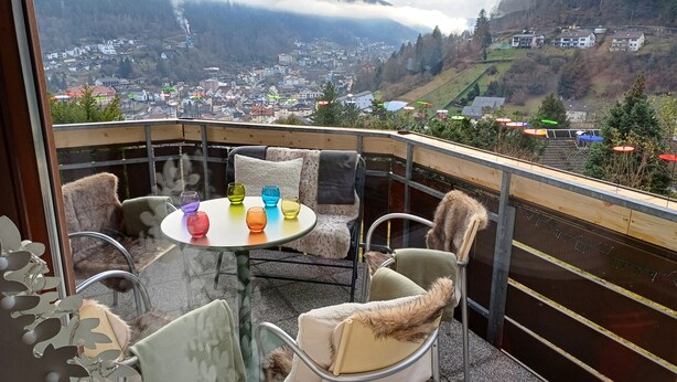 Een balkon met een tafel en stoelen, met uitzicht op een vallei met huizen en bomen.
