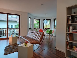 Un vaste espace de vie comprenant un canapé en cuir, une table à manger avec des chaises, une bibliothèque et de grandes fenêtres.