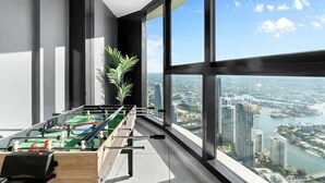 Una habitación moderna con mesa de futbolín, ventanas amplias y vistas a un paisaje urbano.