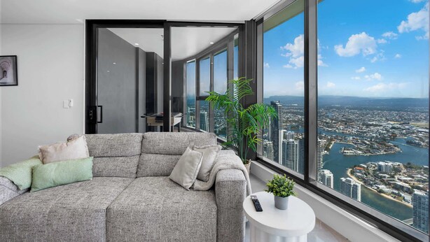 Una sala moderna con un sofá seccional gris, una mesita redonda y un ventanal con vistas a la ciudad.