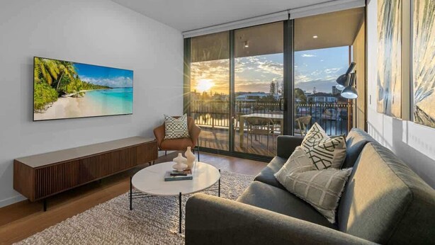 Un salon moderne avec une grande fenêtre, un canapé, une table basse et un tableau représentant une scène de plage.