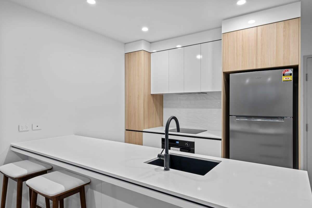 A modern kitchen with a stainless steel refrigerator, white cabinetry, and a black faucet.