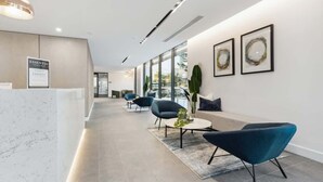 Un espace d’accueil moderne avec un comptoir en marbre, des sièges avec des chaises bleues et des œuvres d’art accrochées aux murs.
