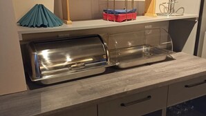 Una kitchenette con un tostador de acero inoxidable, un microondas y un armario de vidrio con platos y tazones.