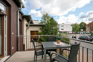 A balcony with a table and chairs, a potted plant, and a view of a street with cars and buildings.