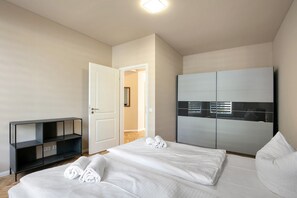Une chambre avec deux lits, une armoire, un meuble pour la télévision et une porte donnant sur une autre pièce.