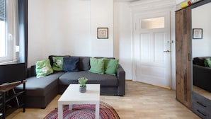 A modern living room with a sectional sofa, a small white table with a plant, and a large mirror. - Apartment "Vogelsberger Bett 5 Die 2 Links" with Wi-Fi (Alsfeld)