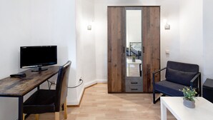 Une pièce comprenant un bureau en bois, une chaise, un canapé, une petite table avec une plante et une armoire avec un miroir.