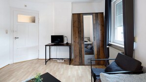 Une pièce comprenant un lit, un bureau avec un ordinateur, une fenêtre avec des rideaux et une porte.