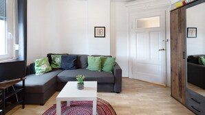 Un salon moderne avec un canapé d’angle, une petite table blanche ornée d’une plante et un grand miroir.