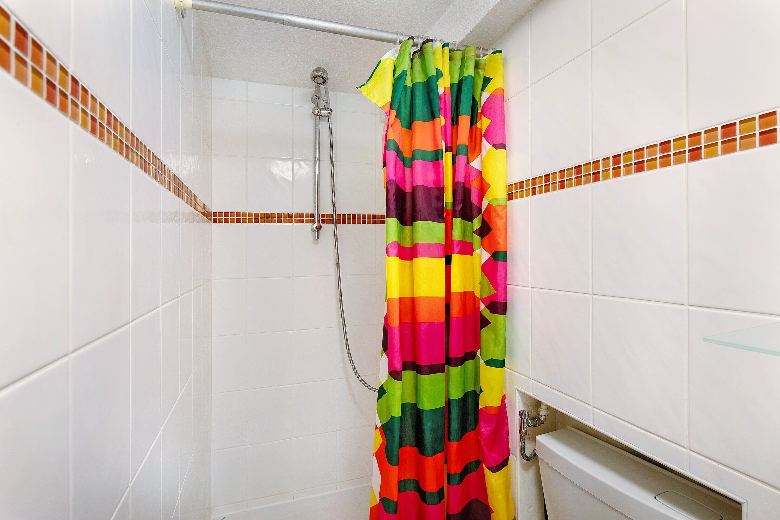 A shower with a colorful curtain, white tiled walls, and a visible showerhead.