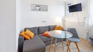 Un salon moderne avec un canapé d’angle gris, une table basse en verre et un téléviseur fixé au mur.