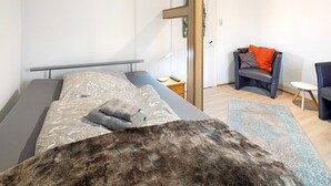 Une chambre à coucher moderne avec un lit, une chaise, une petite table et une porte.