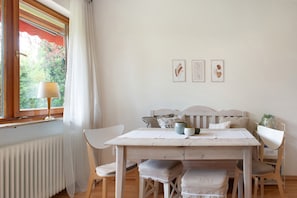 A dining area with a table, chairs, a window with curtains, and wall-mounted artwork.