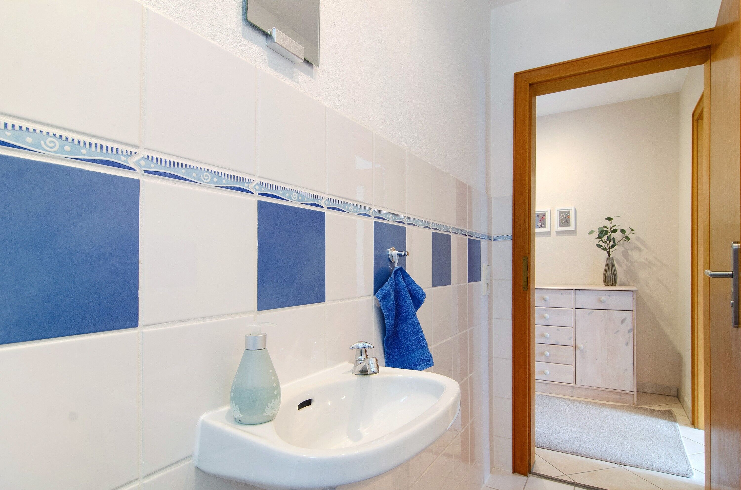 A bathroom with a white sink, blue tiles, a towel, and a cabinet.