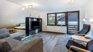 Een moderne woonkamer met een bank, stoelen, een televisie en een groot raam.