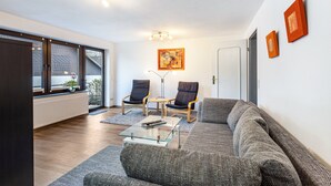 Een moderne woonkamer met een bank, twee fauteuils, een glazen salontafel en een schilderij aan de muur.