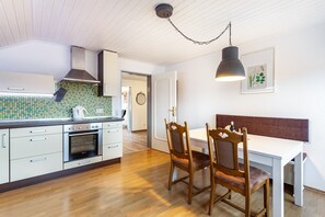 Una cucina con zoccolo in piastrelle, pensili e basi in legno, forno a incasso e zona pranzo con una panca e sedie.