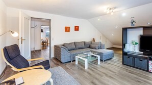 Een moderne woonkamer met een modulaire bank, een glazen salontafel, een tv-meubel en een fauteuil.