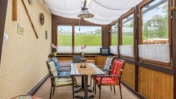 Un porche cubierto con una mesa y sillas, un televisor y vistas a un campo verde.