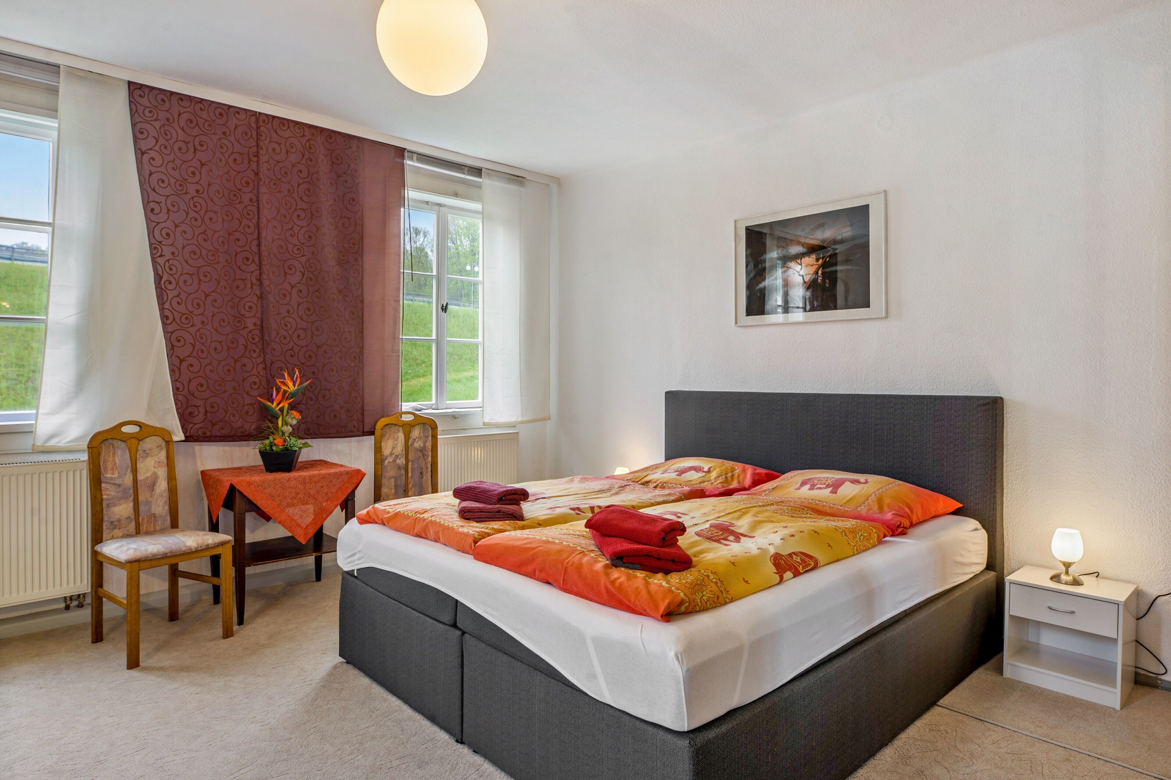 A bedroom with a bed, bedside table, chair, and a window with curtains.
