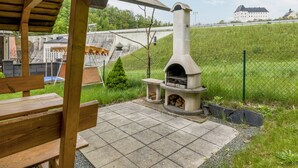 Una chimenea de piedra al aire libre con una chimenea, un banco de madera y un patio empedrado.