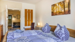 Una habitación de hotel con una cama, un armario, una mesita de noche, una lámpara y un cuadro de un bosque.