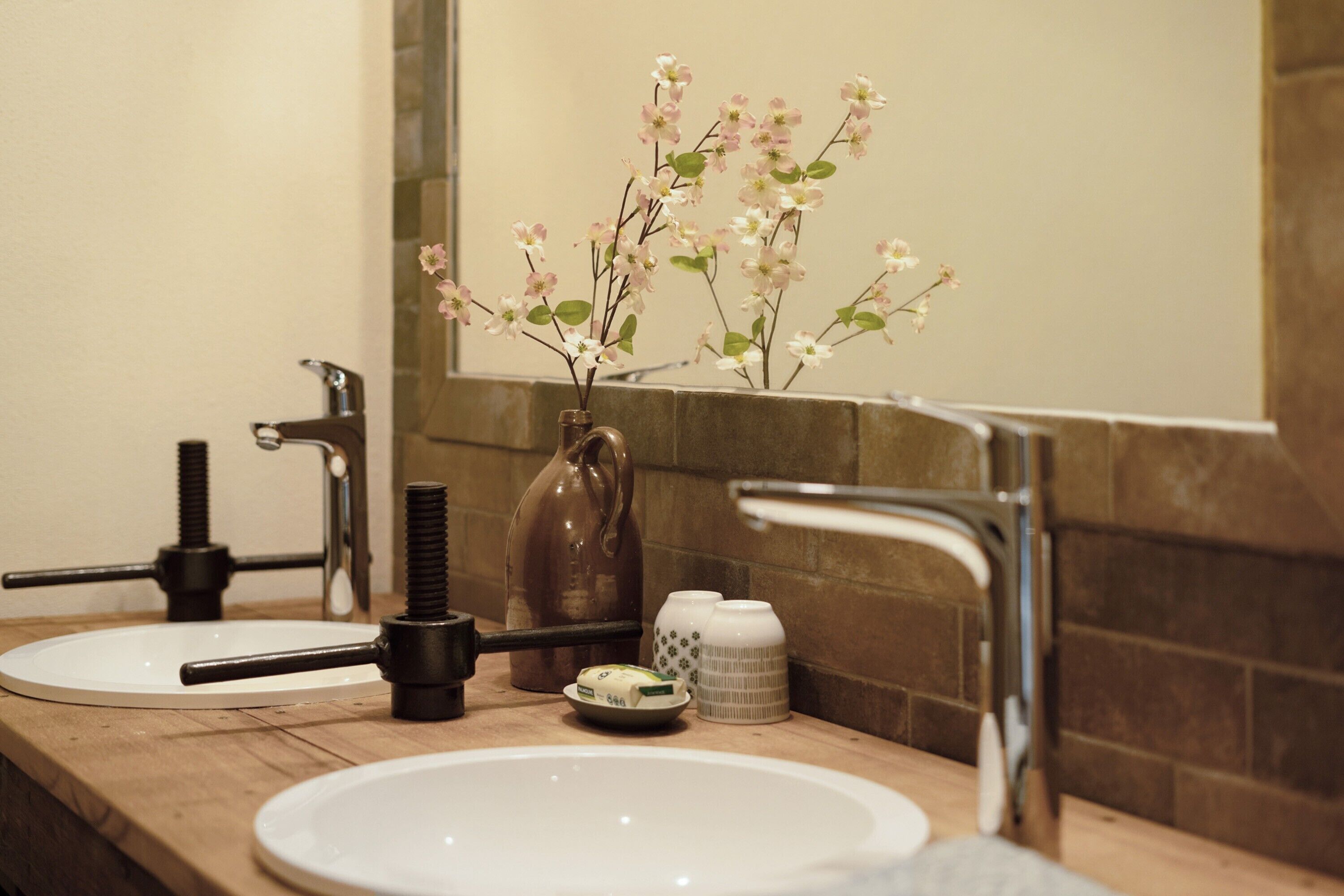 A bathroom with two sinks, a mirror, and a vase with flowers.
