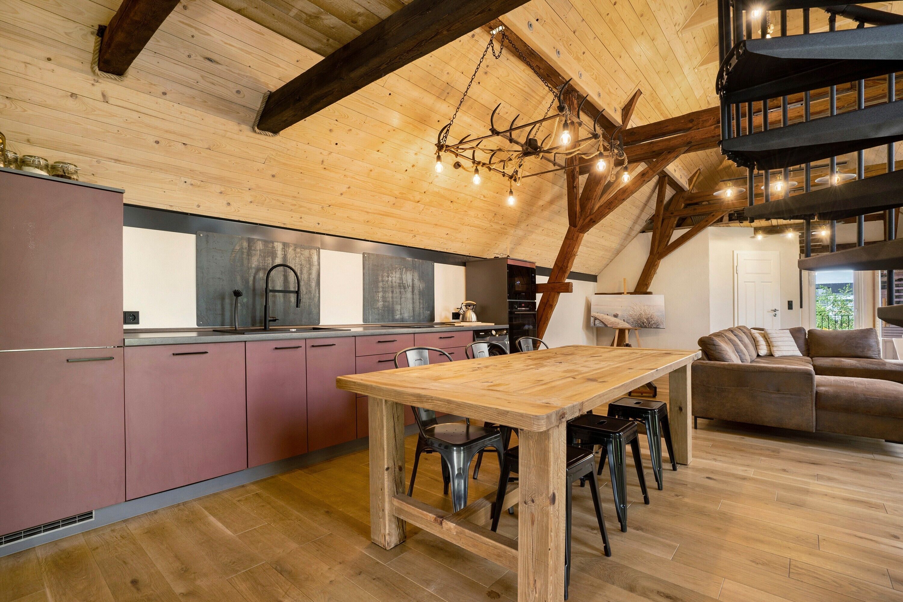 A rustic kitchen with wooden beams, a dining table, and a sofa in a spacious living area.