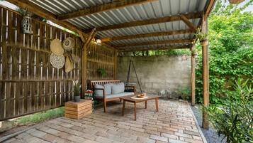 A covered patio with a wooden bench, a table, and hanging planters.