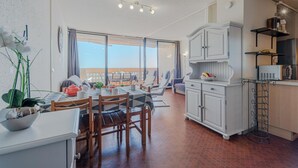 A modern kitchen with white cabinets, a dining area with a table and chairs, and a view through large windows.