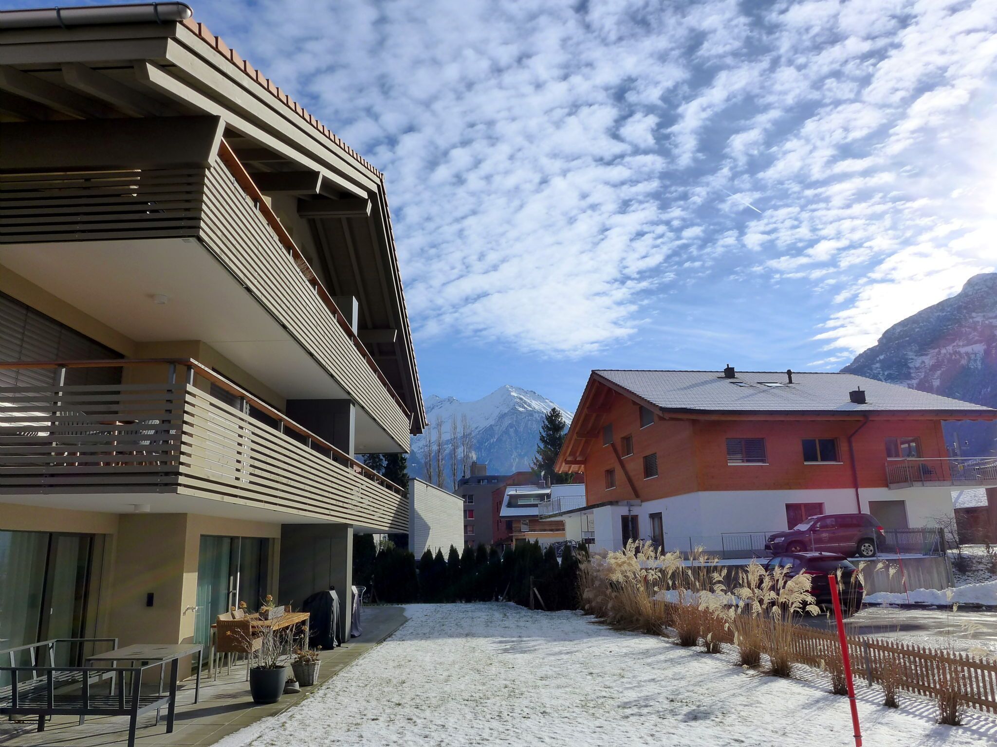Un bâtiment moderne doté d’un balcon, d’un espace extérieur aménagé et couvert, et offrant une vue sur des montagnes enneigées.