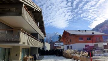 Un bâtiment moderne doté d’un balcon, d’un espace extérieur aménagé et couvert, et offrant une vue sur des montagnes enneigées.