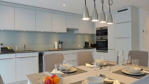 Una cucina moderna con mobili bianchi, un tavolo da pranzo per due persone e una ciotola di frutta sul tavolo.