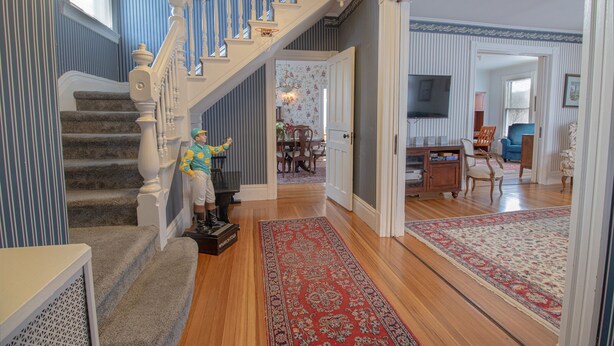 Uma escadaria com corrimão, degraus carpetados e um tapete com padrão vermelho no chão.