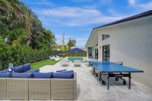 An outdoor area with a ping pong table, wicker furniture, and a pool.