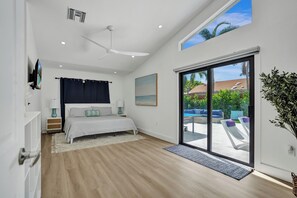 A bedroom with a bed, a ceiling fan, a TV, a window, and a view of the outside.