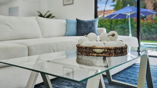Una sala de estar moderna con una mesa de centro de vidrio, un sofá blanco con cojines azules y una cesta de mimbre con adornos.