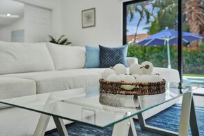 Ein modernes Wohnzimmer mit einem Glastisch, einem weißen Sofa mit blauen Kissen und einem Korbwäscher mit Dekorationsgegenständen.