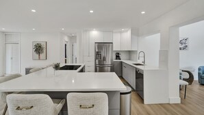 Una cocina moderna con armarios blancos, electrodomésticos de acero inoxidable y una isla central con asientos.