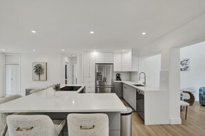 A modern kitchen with white cabinetry, a central island, stainless steel appliances, and a dining area with two chairs.