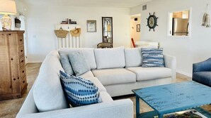 A living room with a white sofa, blue patterned pillows, a wooden cabinet, and a blue coffee table. - Amelia Island 2 Bedroom Oceanfront Private Home (Fernandina Beach)