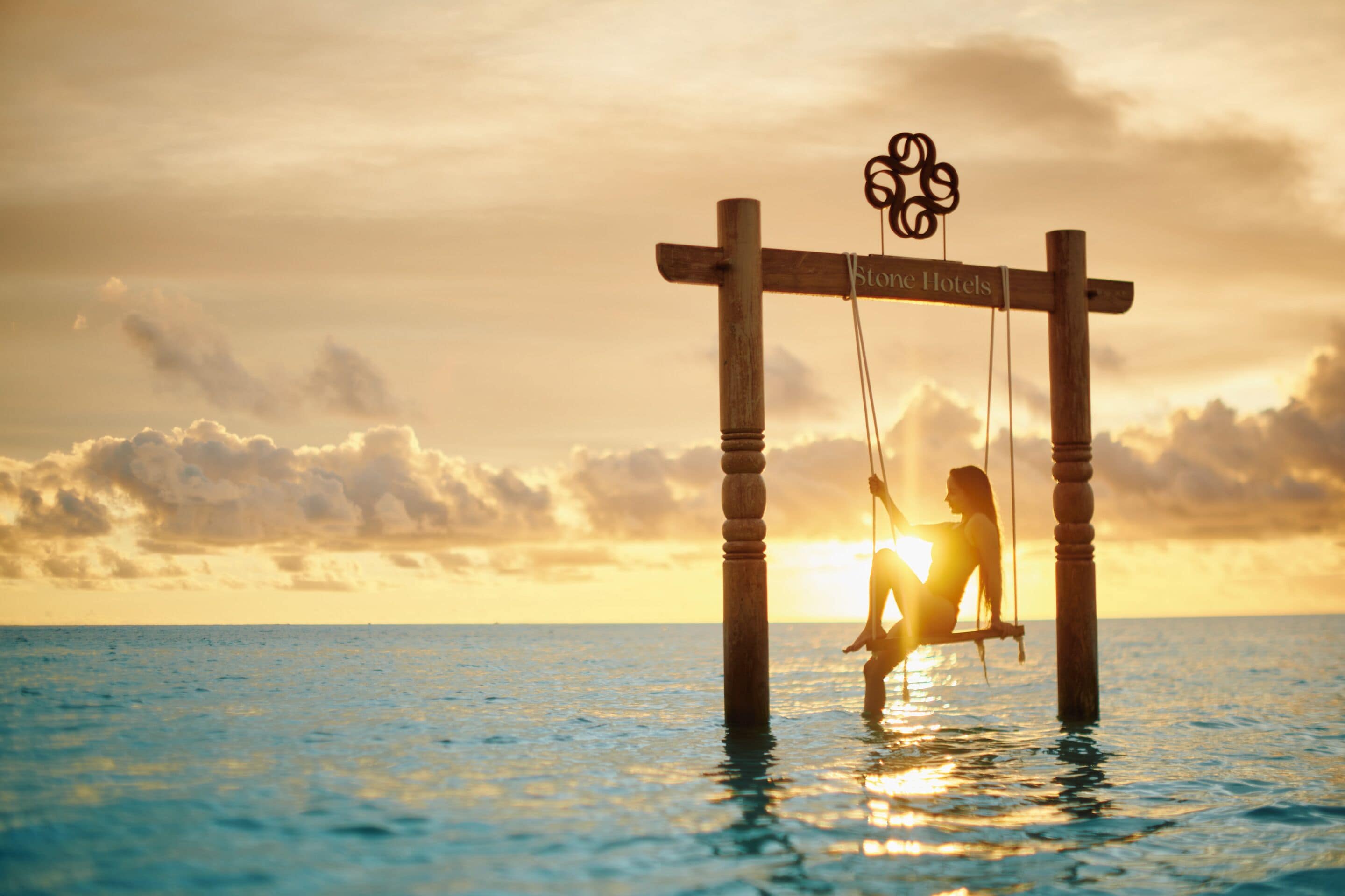 A wooden swing suspended over water with a sign reading "Stone Hotels".