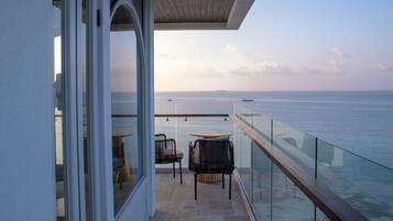 A balcony with a glass railing overlooking the sea, two chairs, and a table.