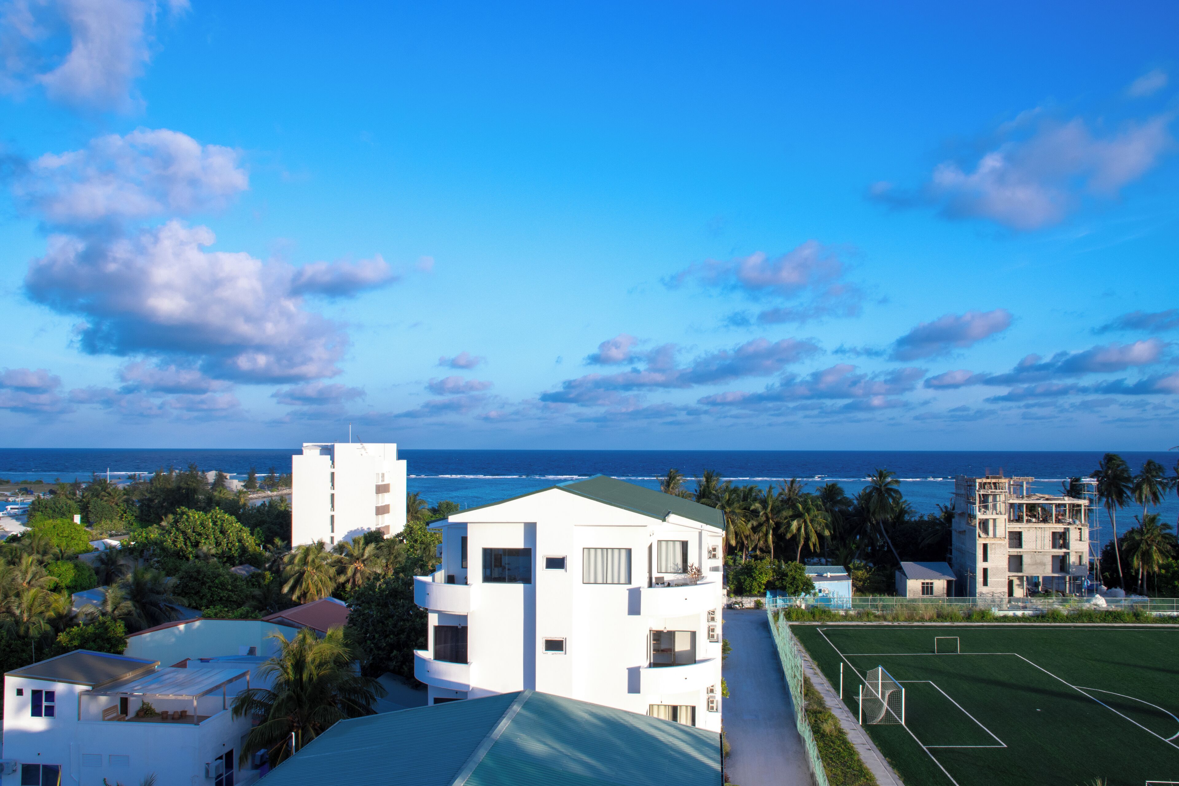 A coastal residential area with modern buildings, a sports field, and a view of the ocean.