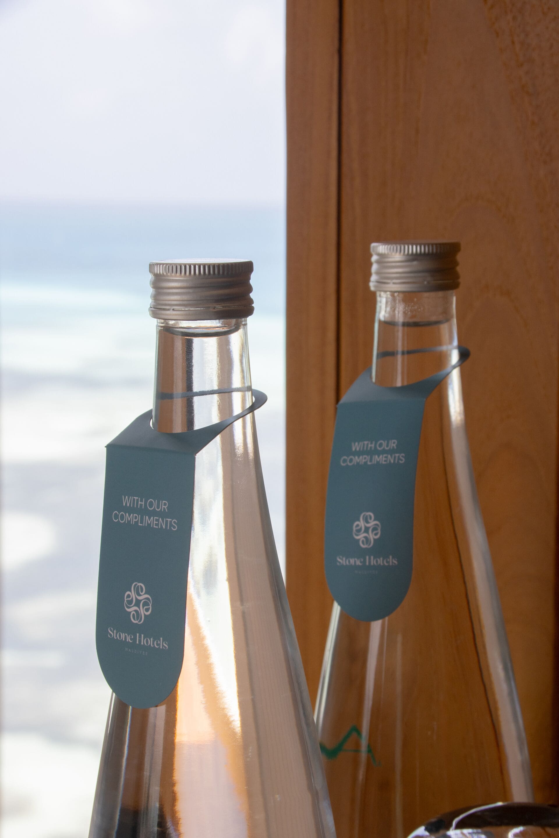 Two glass bottles with metal caps and labels, placed in front of a window with a view of the sky.