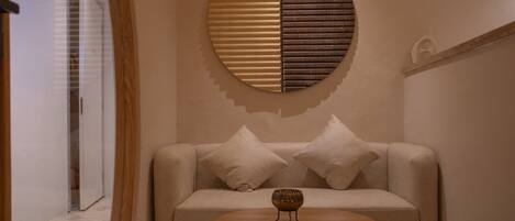 Un soggiorno moderno con un divano beige, due cuscini bianchi, un elemento decorativo rotondo a parete e un piccolo tavolino in legno.