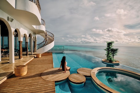 A pool area with wooden deck seating and a view of the ocean.