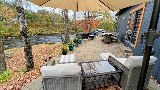 A patio with outdoor furniture, a grill, and a view of a river. - 37PA Superbly appointed riverfront home in LIttleton! Skiing, hiking, firepit, wifi, dog friendly! (Littleton)