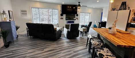 A modern living room with a sofa, chairs, a wooden coffee table, and a bar area with stools.